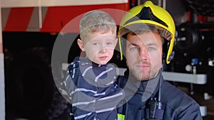 Portrait of firefighter with cute boy on arms. Concept of saving lives, fire safety