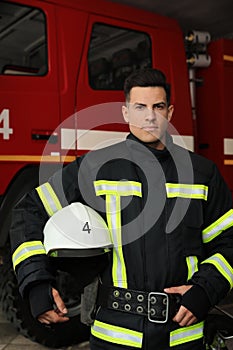 Portrait of firefighter in uniform with helmet near fire truck at station