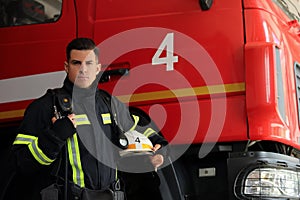 Portrait of firefighter in uniform with helmet near fire truck at station, space for text