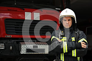 Portrait of firefighter in uniform and helmet near fire truck at station, space for text