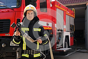 Portrait of firefighter in uniform with high pressure water jet near fire truck outdoors