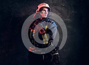 Portrait of a firefighter in uniform and safety helmet holding an oxygen mask and looking sideways with a confident look