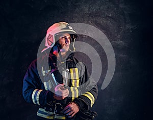 Portrait of a firefighter in uniform and safety helmet holding an oxygen mask and looking sideways with a confident look