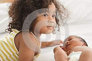 Portrait of first meeting of adorable African little sister and her newborn baby boy on bed at home