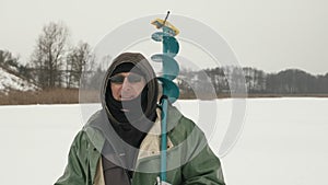 Portrait of fisherman with ice drill on shoulder. Man is walking through frozen river at winter fishing