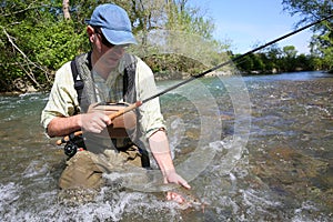 Portrait of fisherman in river catching brown trout