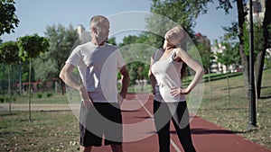 Portrait of fit Caucasian adult couple ending warmup exercise and running away on sports field. Sportive man and woman