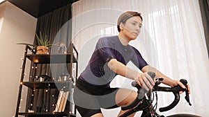 Portrait of fit sportive woman is cycling on indoor smart bike trainer. Professional cyclist is training on exercise bicycle. Indo