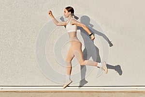 Portrait of fit sporty girl jumping over in the air looking straight ahead, having good stretching  on gray background