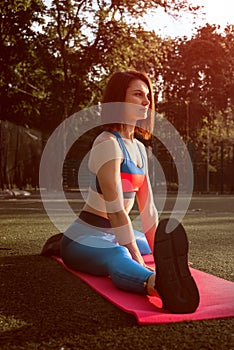 Portrait of fit and sporty young woman doing exercises of stretching, yoga or pilates in the early morning park