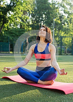 Portrait of fit and sporty young woman doing exercises of stretching, yoga or pilates in the early morning park.