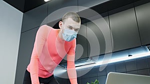Portrait of fit young man athlete in protective medical mask training at home on stationary bicycle during quarantine. Sportive gu