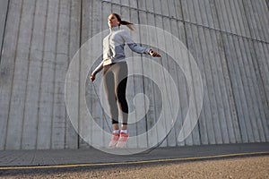 Portrait of fit young woman with jump rope outdoors. Fitness female doing skipping workout outdoors on sunrise or sunset