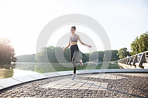 Portrait of fit young woman with jump rope in a park. Fitness female doing skipping workout outdoors on a sunny day.