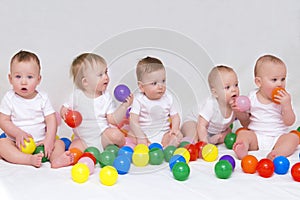 Portrait of five cute babies on light background playing with colorful balls