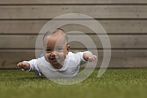 Portrait of a five months old baby girl lying on her belly outside on artificial grass