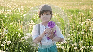 portrait of a five year old boy in a hat stands on a field of dandelions and shoots soap bubbles from a toy gun at