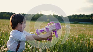 portrait of a five year old boy in a hat stands on a field of dandelions and shoots soap bubbles from a toy gun at