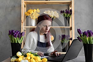 Portrait of a florist in an apron, working in her own flower shop, using a laptop organizing logistics and delivery