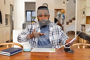 Portrait of focused african american man having video call and holding document at home