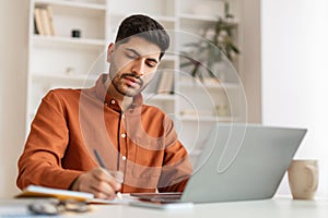 Portrait of focused Arab man using pc and writing