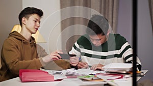 Portrait of focused Asian boy doing lessons as his Caucasian groupmate annoying him. Teenager showing something to