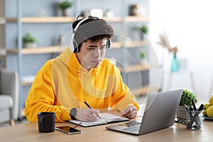 Focused asian man working on laptop and writing