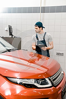 portrait of focused auto mechanic with notepad examining car