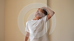 Portrait of focused little kid girl stretching neck and wrist muscles for exercise during home workout standing in light