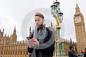 Portrait of a focused man with a smartphone in his hands against the backdrop of the London Big Ben tower.