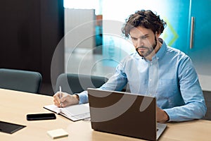 Portrait of focused man using laptop and writing in notebook