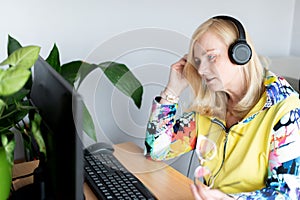 Portrait of focused middle-aged woman wearing headphones watching webinar at office computer