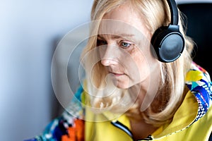 Portrait of focused middle-aged woman wearing headphones watching webinar at office computer