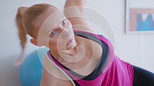 Portrait of focused sportswoman exercising in side plank position. Young strong Caucasian woman training indoors