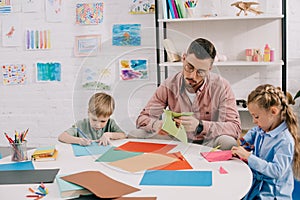 portrait of focused teacher and preschoolers cutting colorful papers with scissors