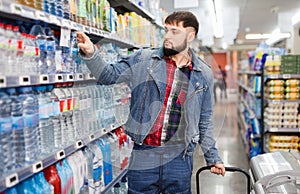 Portrait of focused young man purchasing bottled water in grocery store