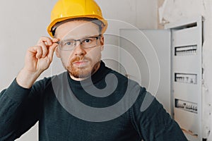 Portrait foreman man in yellow helmet inspecting electrical panel and work of electrician in apartment