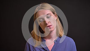 Portrait of formally-dressed tired woman watching into camera with passivity on black background.