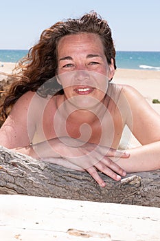 Portrait of a forty woman on sand sea in swimsuit behind driftwood on beach of Lacanau France