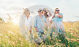 Portrait of four cheerful smiling and laughing women embracing during outdoor walking by high green grass hill. They looking at