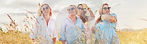 Portrait of four cheerful smiling and laughing women during outdoor walking by a high green grass hill. They looking at the camera