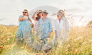 Portrait of four cheerful smiling and laughing women during outdoor walking by a high green grass hill. They looking at the camera