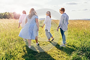 Portrait of four cheerful smiling women holding hand in hand walking by a high green grass meadow. They looking at the camera.