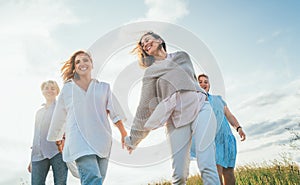 Portrait of four cheerful smiling women holding hand in hand walking by a high green grass meadow. They looking at the camera.