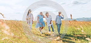 Portrait of four cheerful smiling women holding hand in hand walking by a high green grass meadow. They looking at the camera.