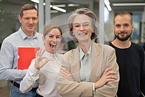 Portrait of four office workers. A gray-haired mature woman, a Caucasian man, a bearded man and a red-haired woman.