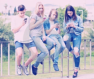 Portrait of four teenagers sitting with their mobile phones outd