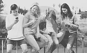 Portrait of four teenagers sitting with their mobile phones outd