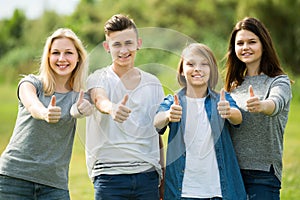 Portrait of four teenagers standing and holding thumbs up together outdoors