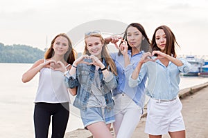 Portrait of four young student girls showing finger gesture heart. Beautiful happy young women on the waterfront